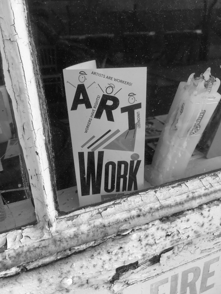 Praxis' newest leaflet seen through the window of Rebel Reads - "ART WORK"